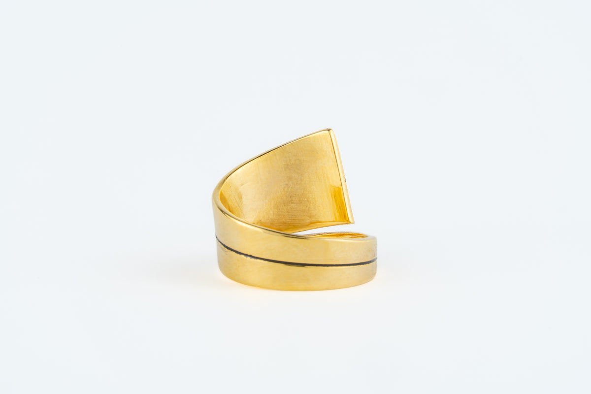 A gold-plated open wrap ring with a wide, curved triangular top and a thin dark line detail, shown on a plain white background.