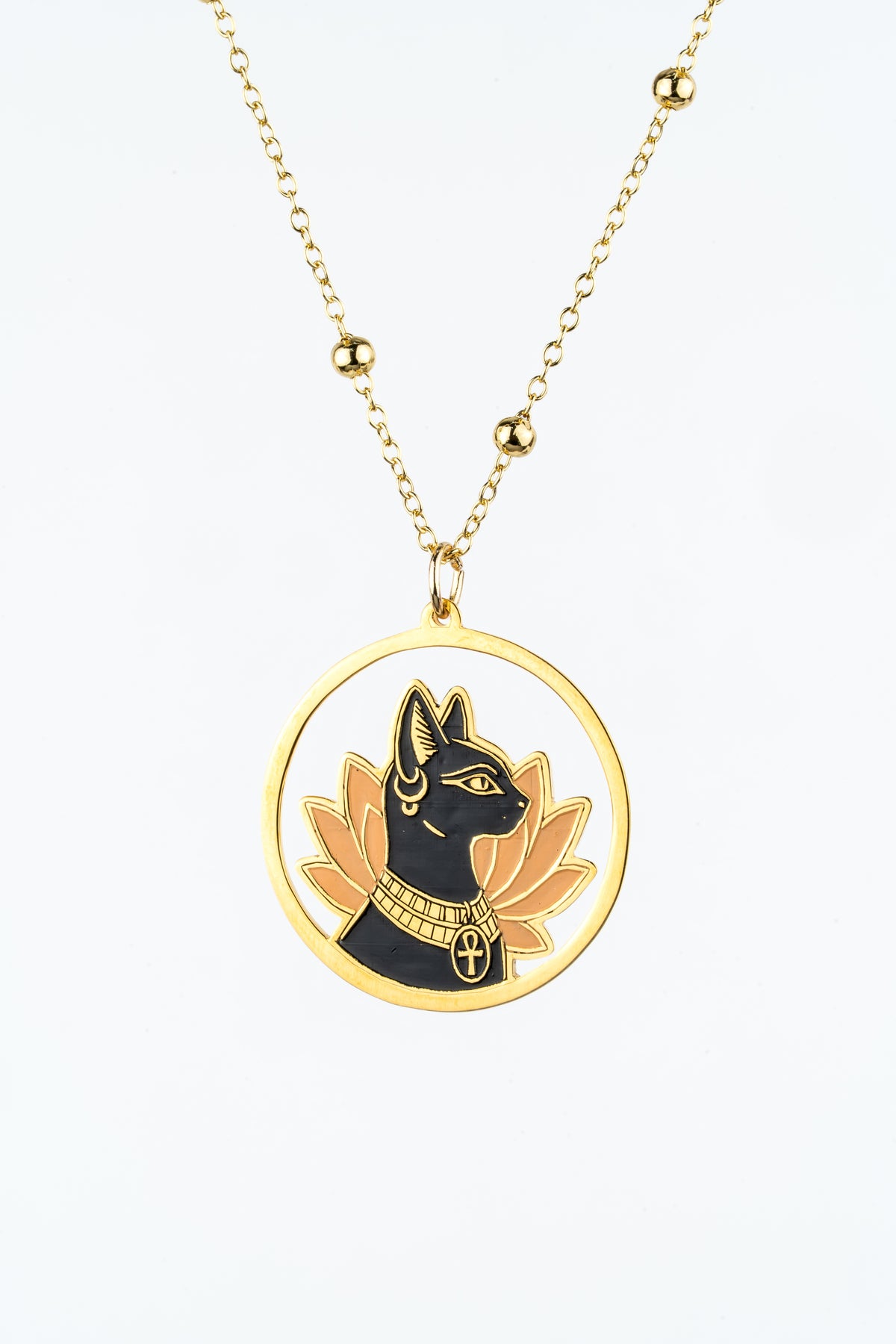 A gold pendant necklace featuring a circular medallion with a black cat profile (inspired by ancient Egyptian Bastet), gold lotus petals on a white background.