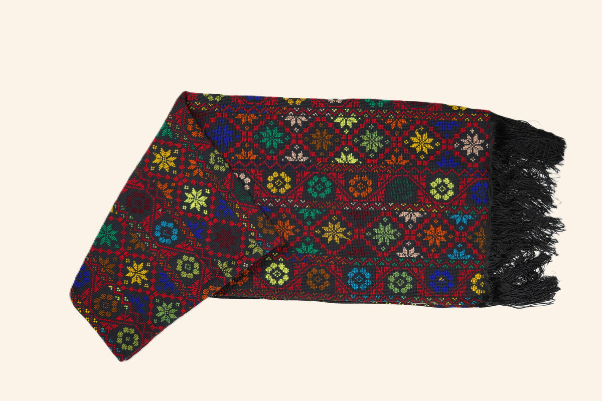 A hand embroidered shawl with intricate multicolor geometric and floral patterns, finished with black fringe , displayed on a solid light beige background.