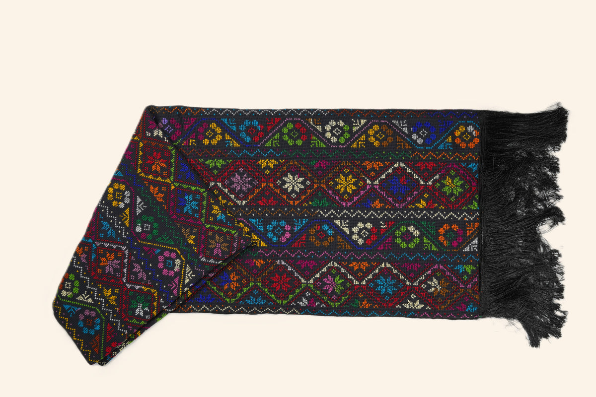 A hand embroidered Sinai shawl with intricate multicolor geometric and floral patterns, finished with black fringe, displayed on a solid light beige background.