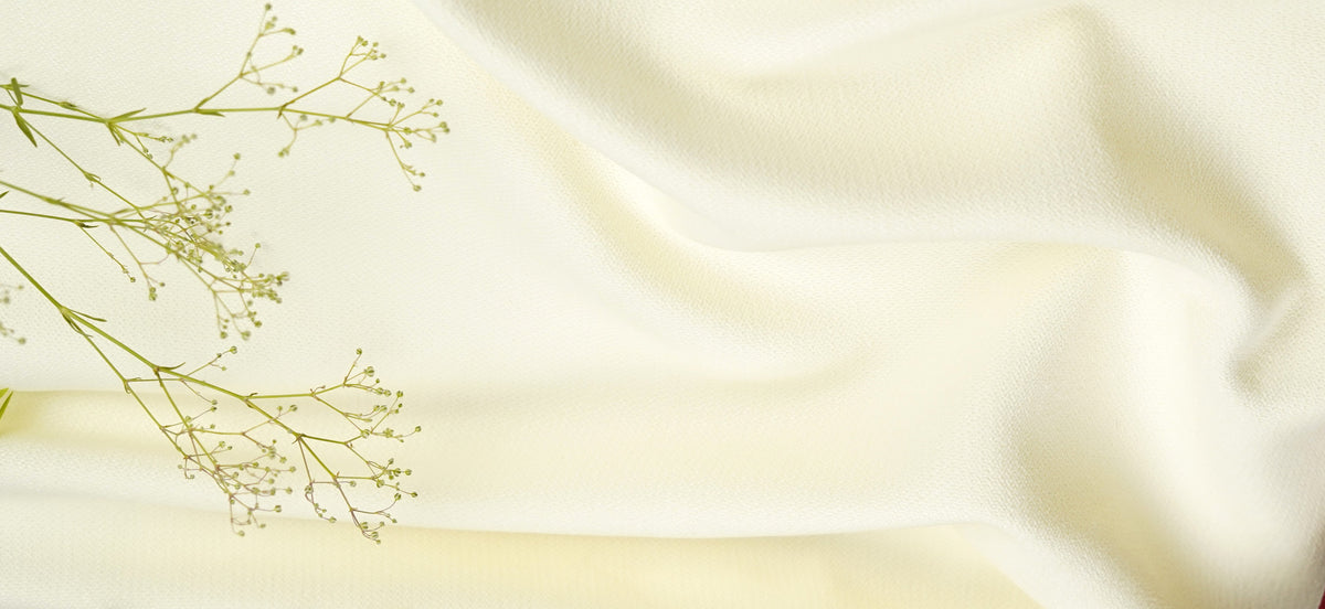 Cream-colored draped fabric with delicate baby's breath flowers on the left side, creating a soft, elegant background.