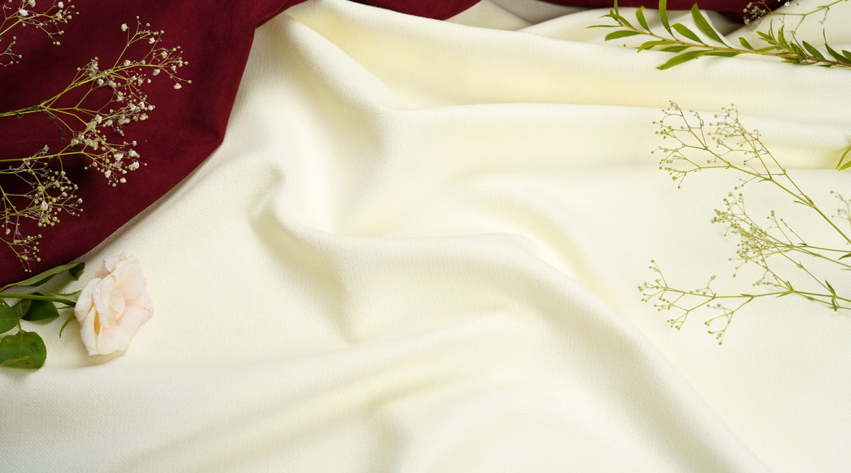 A draped cream-colored fabric,, styled with a deep burgundy velvet cloth, a pale pink rose, and delicate baby's breath flowers.