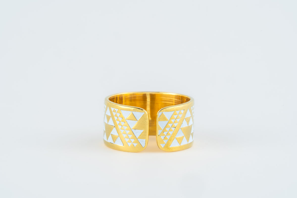 A gold-plated open band ring with white geometric triangle patterns on the front, photographed on a clean white background.