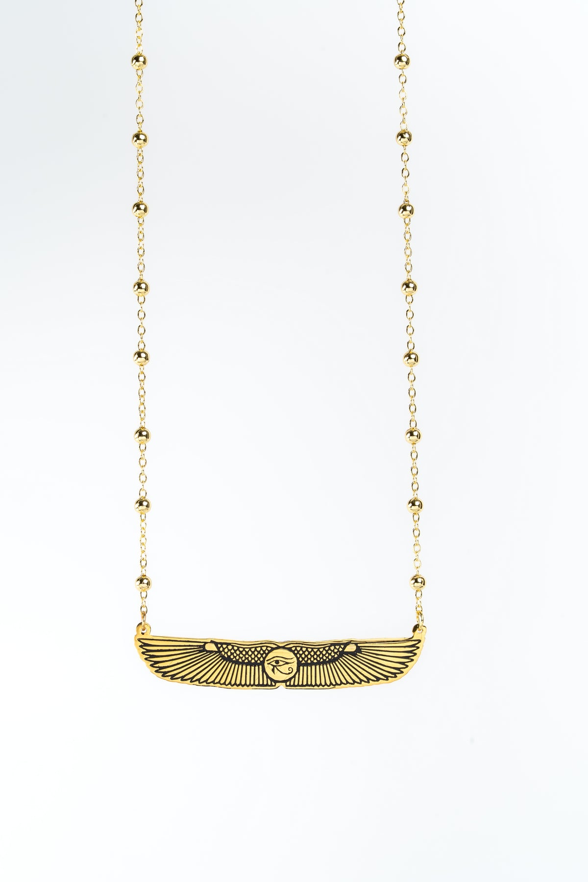 A gold-plated pendant necklace featuring a winged eye of Horus design , suspended from a beaded chain against a plain white background.